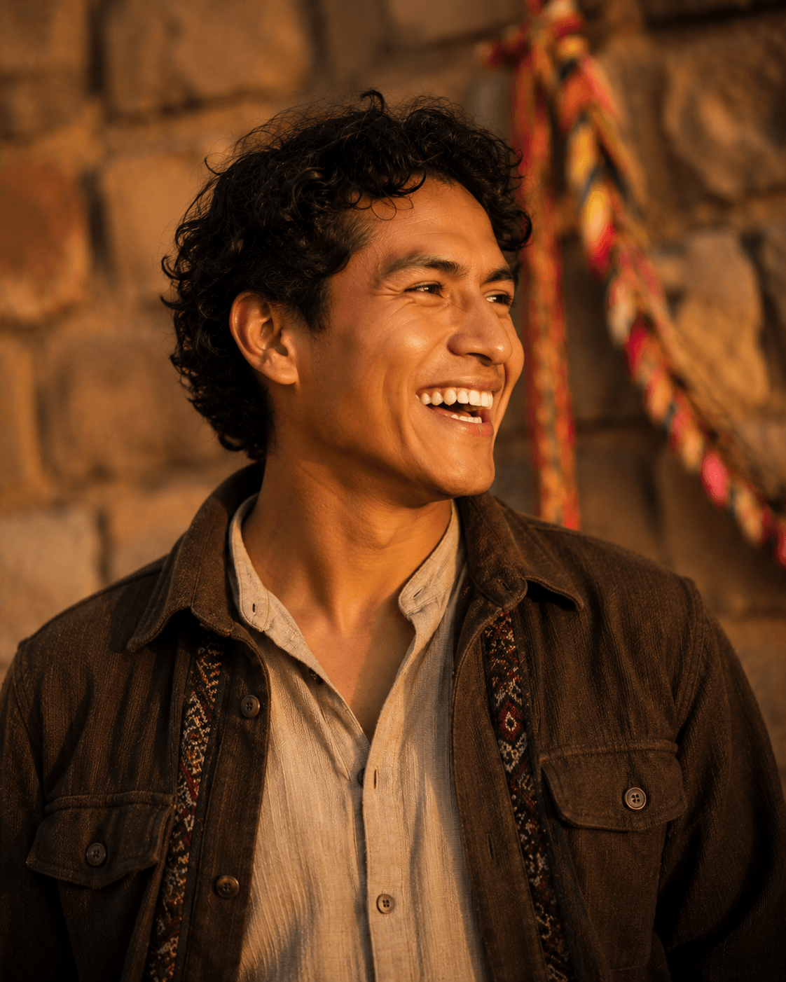 Portrait of El Tinku — young Bolivian man with curly hair, caught mid-laugh, looking off-camera.
