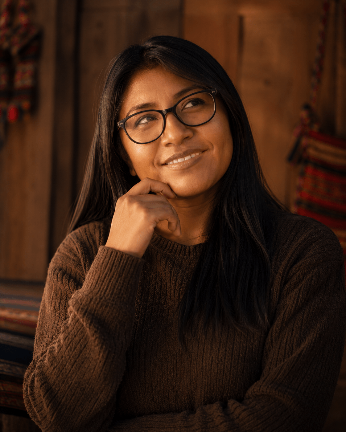 Portrait of La Awicha — young Bolivian woman with glasses, hand near her chin, contemplative smile.