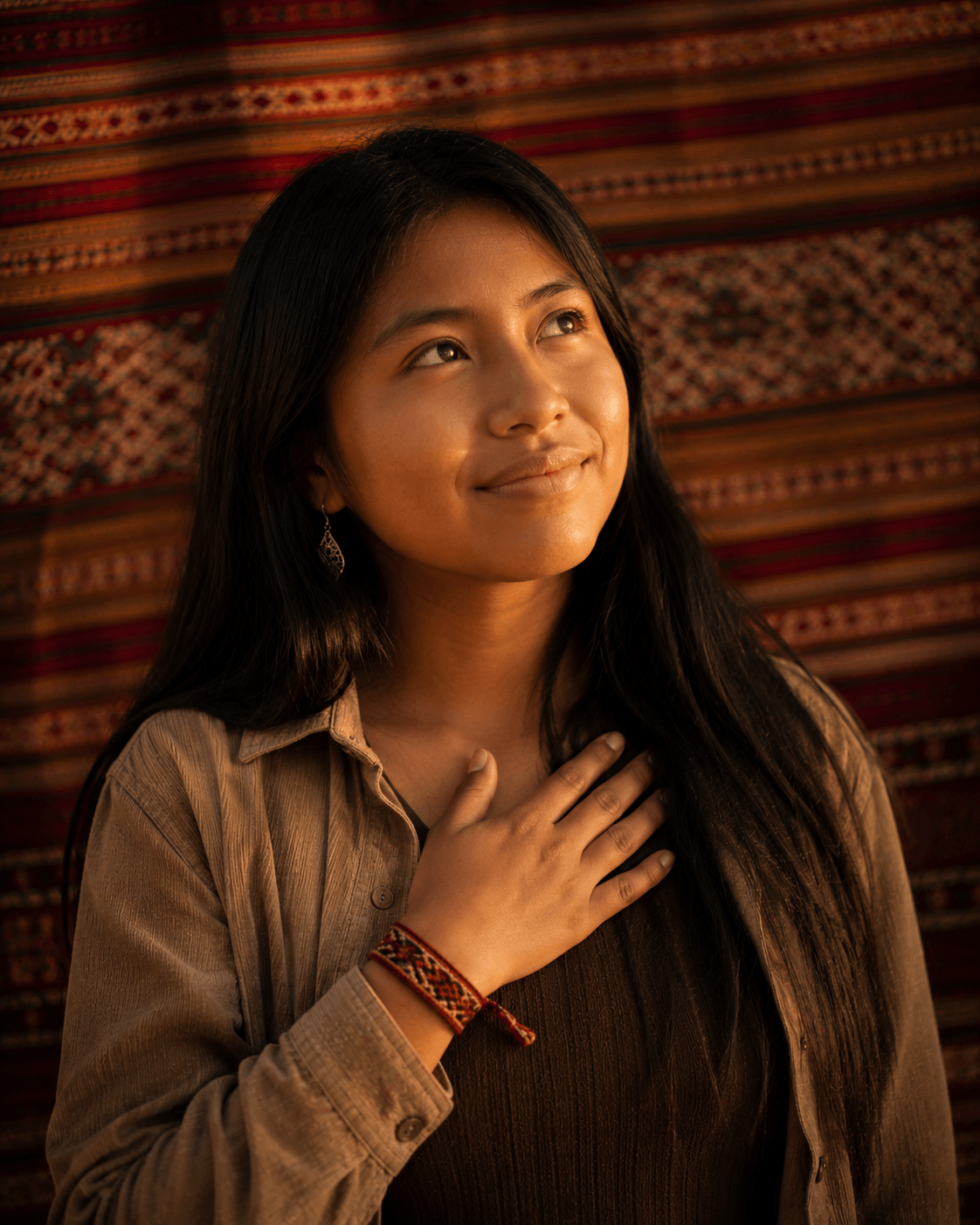 Portrait of La Wayra — young Bolivian woman with one hand resting on her chest, looking upward with a soft proud smile.